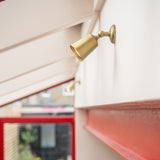 Antique Brass Bayliss Single 50mm Spotlight fitted  to a white wall on the right with red metal beam beneath. 
